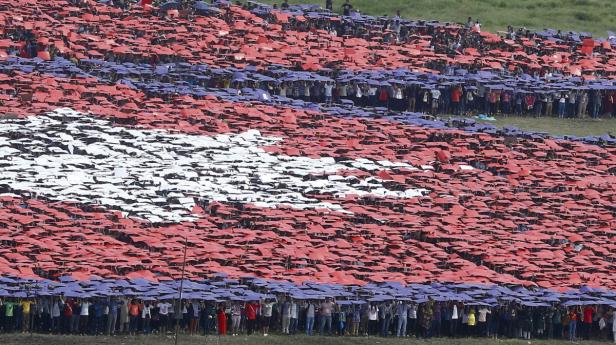 Viele Menschen halten farbige Schirme hoch, um die nepalesische Flagge zu bilden.