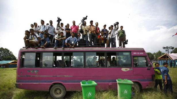 Eine Gruppe von Reportern und Fotografen sitzt auf dem Dach eines pinkfarbenen Busses.