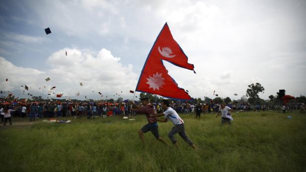 Zwei Männer rennen mit der nepalesischen Flagge über eine Wiese, während Drachen steigen.