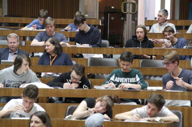 Mehrere Personen sitzen in einem Hörsaal und schreiben an ihren Tischen.