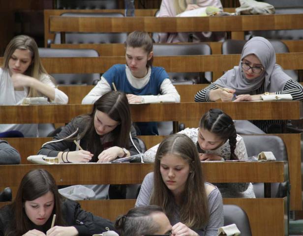 Mehrere Studentinnen sitzen in einem Hörsaal und schreiben mit Stiften.