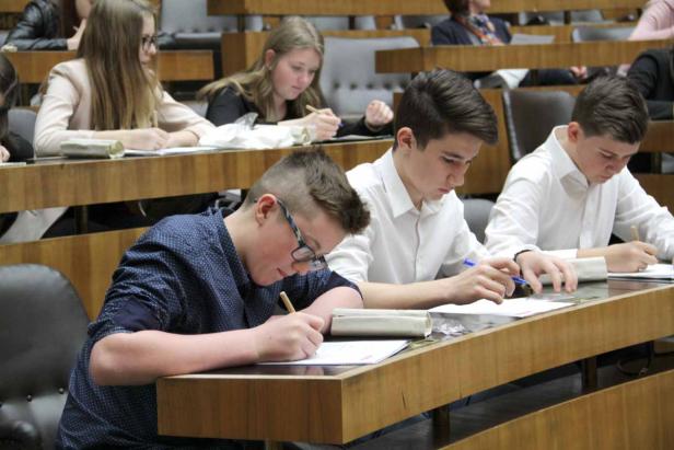 Schüler sitzen in einem Hörsaal und schreiben an ihren Tischen.