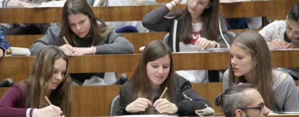 Mehrere Studentinnen sitzen in einem Hörsaal und schreiben mit Stiften auf Papier.