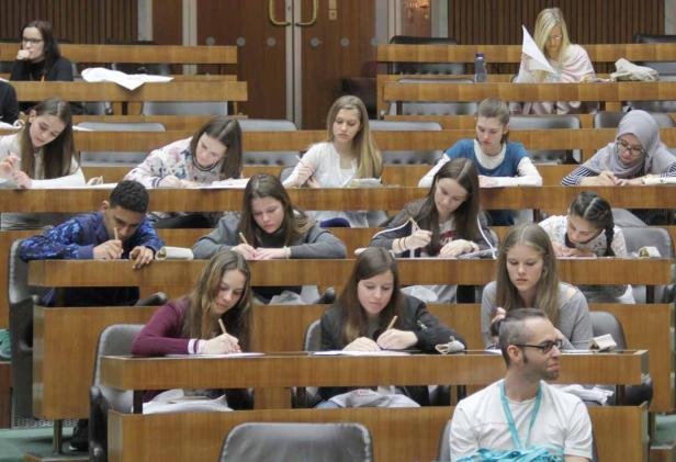 Schüler und ein Lehrer sitzen in einem Hörsaal und schreiben an ihren Tischen.