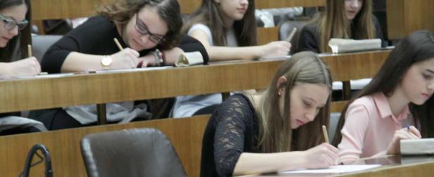 Mehrere Schülerinnen sitzen in einem Klassenzimmer und schreiben an ihren Tischen.