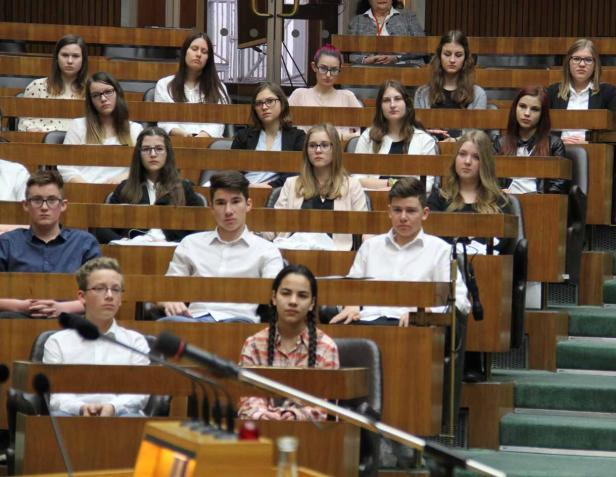 Eine Gruppe Jugendlicher sitzt in einem holzvertäfelten Raum, möglicherweise ein Parlament.