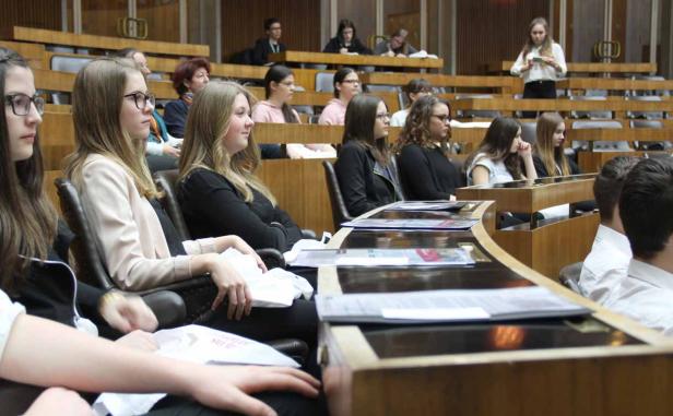 Eine Gruppe junger Leute sitzt in einem Hörsaal oder Parlament.