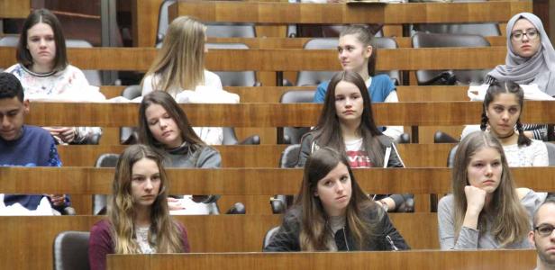 Eine Gruppe von Jugendlichen sitzt in einem Hörsaal oder Gerichtssaal.