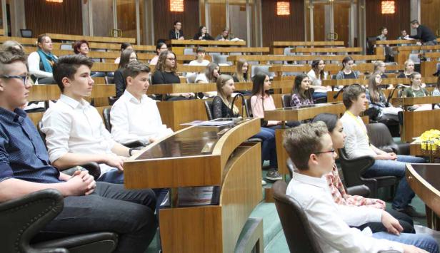 Eine Gruppe junger Leute sitzt in einem großen Saal mit Holzbänken.