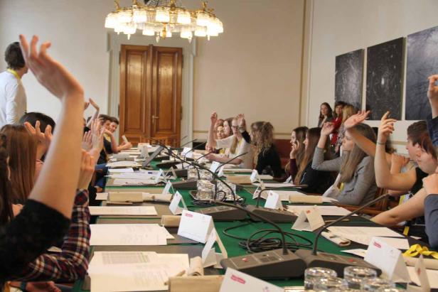 Eine Gruppe junger Leute sitzt an einem Tisch und hebt die Hände.