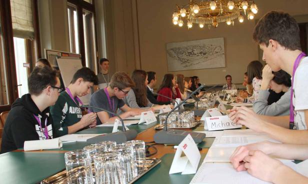 Jugendliche sitzen an einem langen Tisch mit Mikrofonen und Namensschildern.