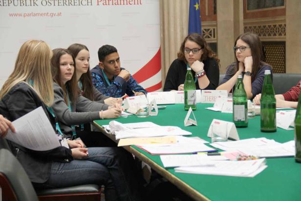 Eine Gruppe junger Leute sitzt an einem Tisch im österreichischen Parlament.