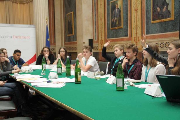 Eine Gruppe Jugendlicher sitzt an einem Tisch im österreichischen Parlament und diskutiert.