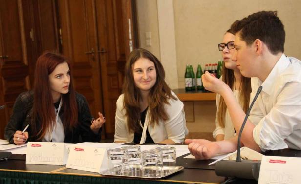 Junge Leute sitzen an einem Tisch und diskutieren während einer Konferenz.