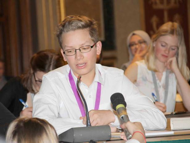 Ein junger Mann spricht bei einer Konferenz in ein Mikrofon.