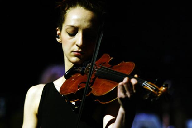 Eine junge Frau spielt auf einer dunklen Bühne Violine.