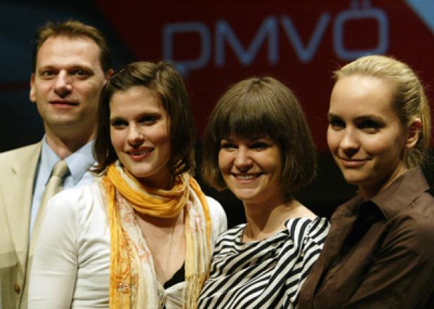 Eine Gruppe von vier Personen posiert vor einem roten Hintergrund mit dem Schriftzug „DMVÖ“.