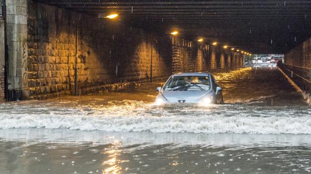 Ein Auto fährt durch eine überflutete Unterführung.