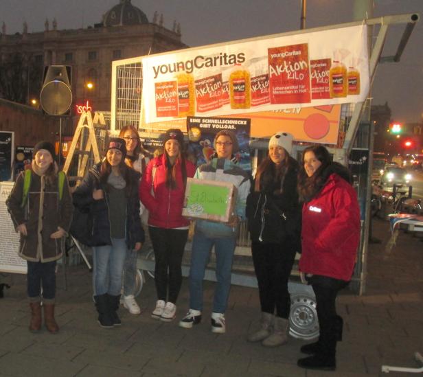 Eine Gruppe junger Leute steht vor einem Stand der „Young Caritas“ mit einer Spendenbox.