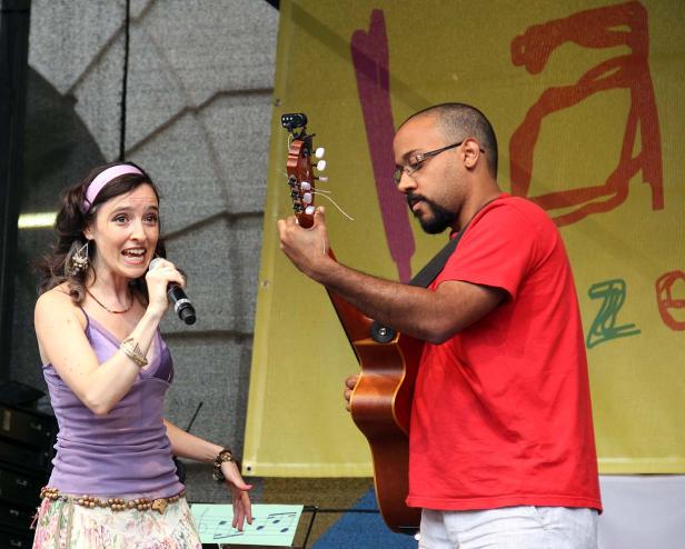 Eine Sängerin mit Mikrofon und ein Gitarrist treten auf einer Bühne auf.