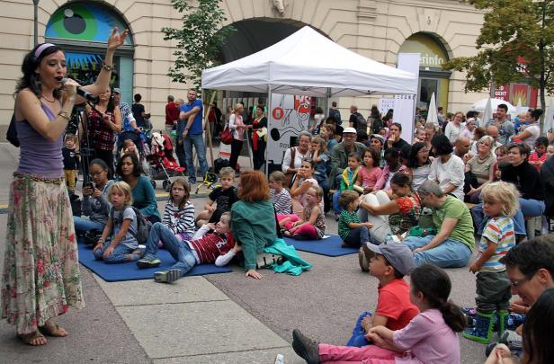Eine Frau singt vor einer Gruppe von Kindern und Erwachsenen im Freien.
