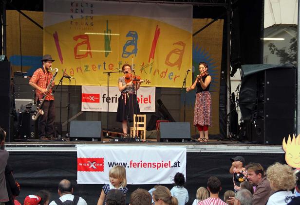 Drei Musiker spielen auf einer Bühne vor Publikum bei einem „lalala konzerte für Kinder“-Event.