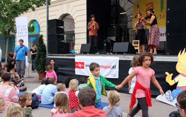 Kinder sitzen vor einer Bühne, auf der eine Band spielt.