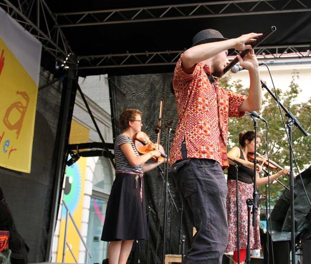 Eine Band spielt auf einer Bühne mit Geigen und einem Blasinstrument.