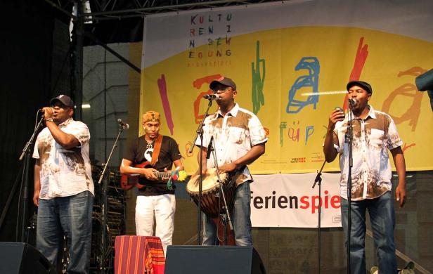 Eine Musikgruppe tritt auf einer Bühne vor einem gelben Banner auf.