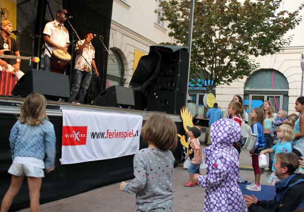 Eine Band spielt auf einer Bühne vor einer Gruppe von Kindern.