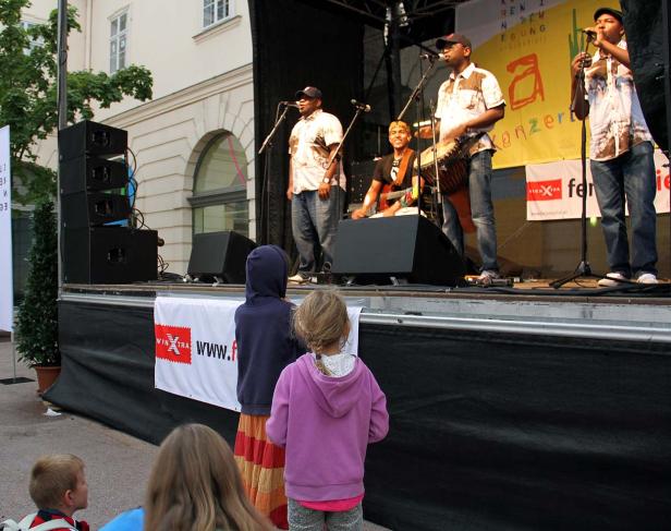 Eine Band spielt auf einer Bühne vor einem Publikum im Freien.