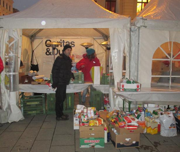 Ein Stand der Caritas mit Helfern und gespendeten Lebensmitteln unter einem Zelt.