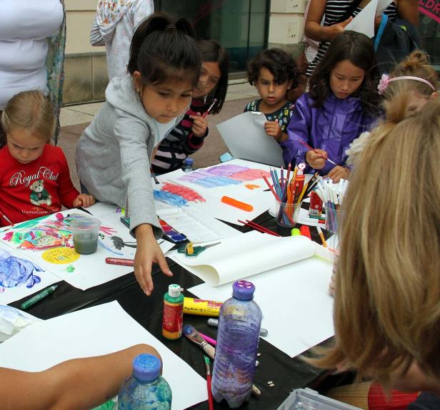 Mehrere Kinder malen und zeichnen an einem Tisch im Freien.