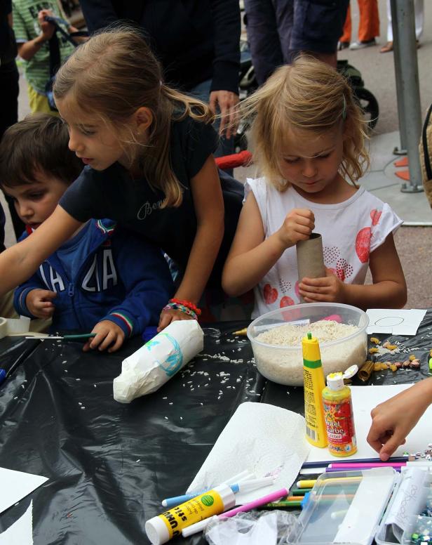 Kinder basteln mit Reis, Papier und Klebstoff an einem Tisch.
