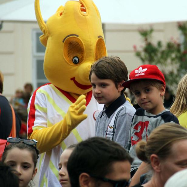 Ein gelbes Maskottchen steht neben zwei Jungen in der Menschenmenge.