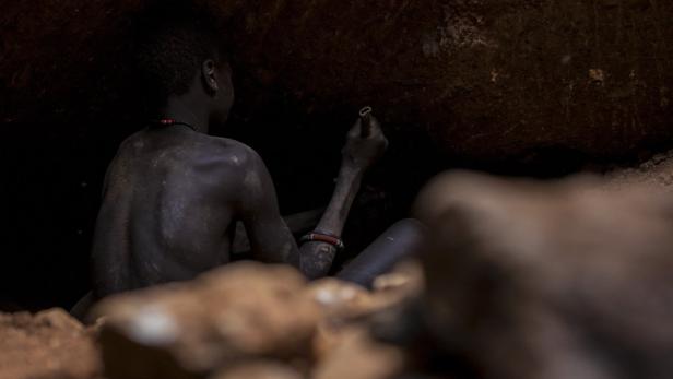Ein Mann mit traditionellem Schmuck zeichnet in einer dunklen Höhle an die Wand.