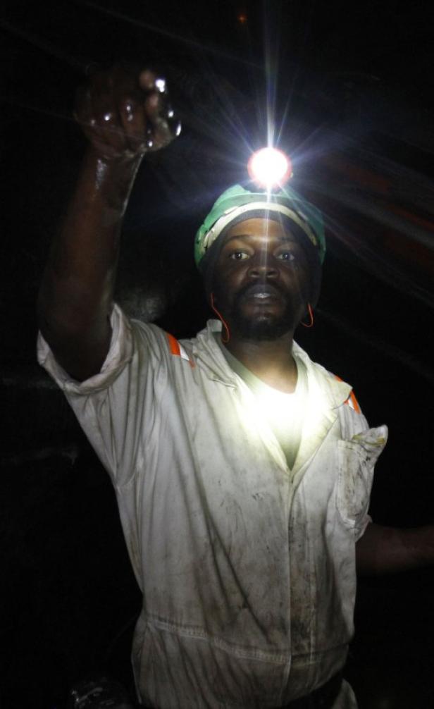 Ein Bergmann mit Helm und Stirnlampe in einem dunklen Schacht.