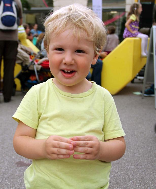 Ein lächelnder Junge mit blonden Haaren steht im Vordergrund.