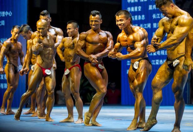 Eine Reihe von Bodybuildern posiert auf einer Bühne während eines Wettkampfs.