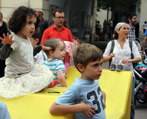 Eine Gruppe von Kindern und Erwachsenen versammelt sich im Freien an einem sonnigen Tag.