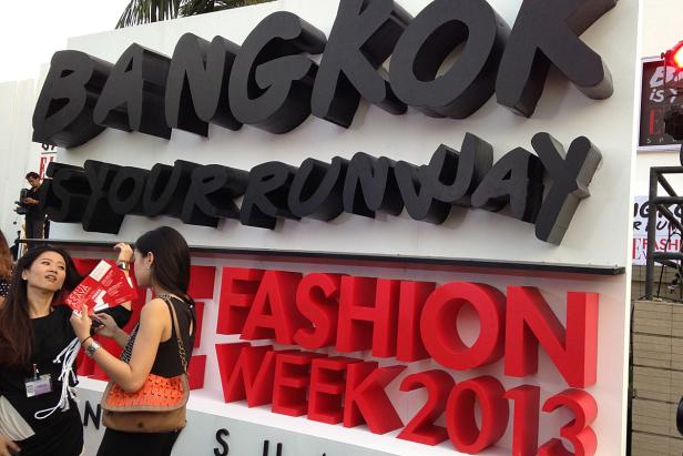 Zwei Frauen stehen vor einer Werbetafel für die Bangkok Fashion Week 2013.