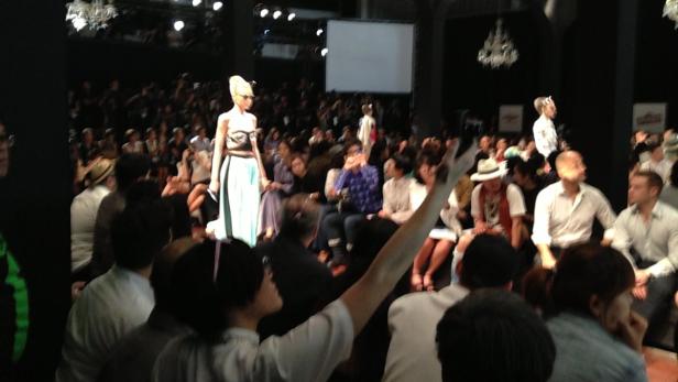 Eine Frau präsentiert Mode auf einem Laufsteg vor Publikum.