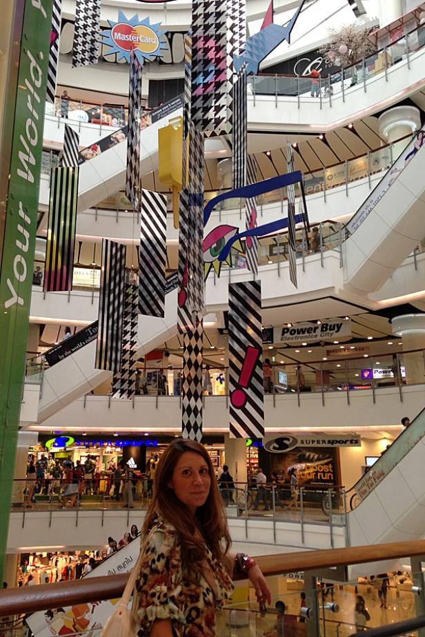 Eine Frau steht in einem Einkaufszentrum mit mehreren Etagen und dekorativen Hängeelementen.