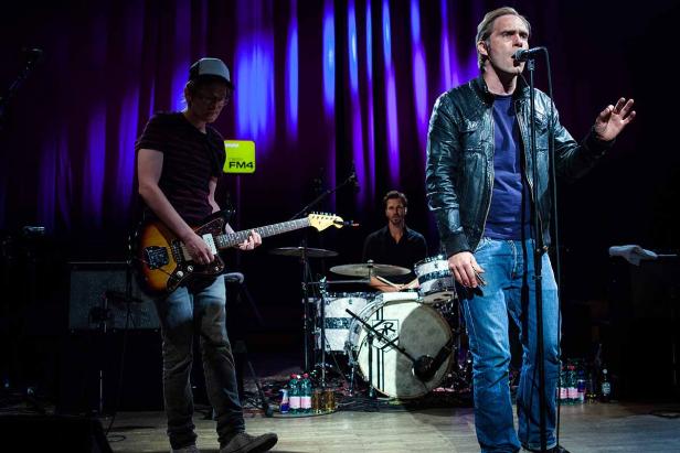 Eine Band tritt auf einer Bühne mit blauem Hintergrund auf.
