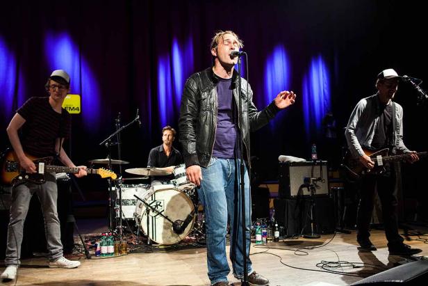 Eine Band tritt auf einer Bühne vor einem dunklen Vorhang auf.