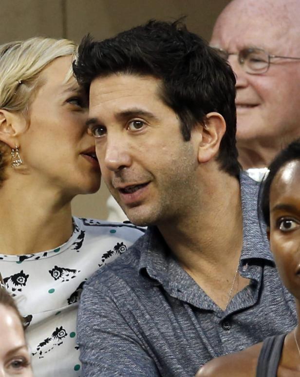 David Schwimmer wird von einer Frau etwas ins Ohr geflüstert.