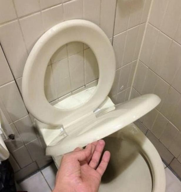 Eine Hand berührt einen Toilettensitz in einem Badezimmer.