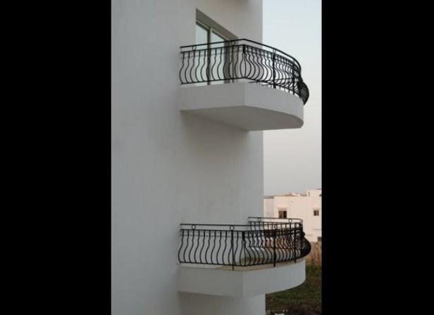 Zwei kleine Balkone mit schwarzen Geländern an einer weißen Fassade.