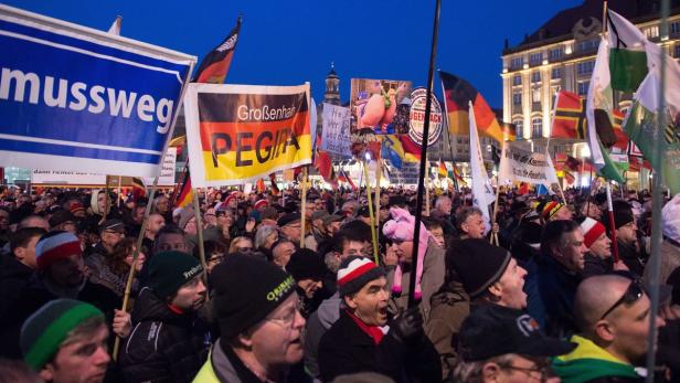 Eine Menschenmenge demonstriert mit Deutschlandfahnen und Schildern, darunter eines von Pegida.