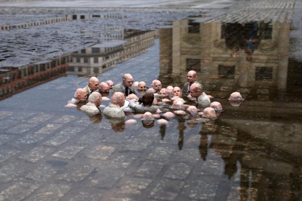 Eine Gruppe von Skulpturen, die in einer Wasserpfütze auf einem gepflasterten Platz stehen.